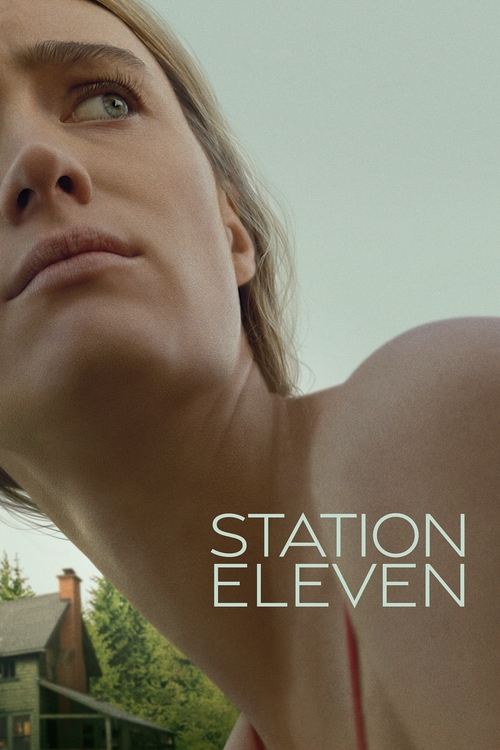 This is a vertical poster for the limited series "Station Eleven." The image is a close-up, low-angle shot looking up at the chin and neck of a blonde woman with blue eyes, who is looking out of frame. The perspective distorts the view, showing her skin texture and the shape of her jawline against a pale, desaturated sky. The background, visible in the lower-left, is a small, blurred wooden house with a chimney and green pine trees. In the lower-right corner, the title "STATION ELEVEN" is rendered in a thin, sans-serif, mint-green font over two lines.