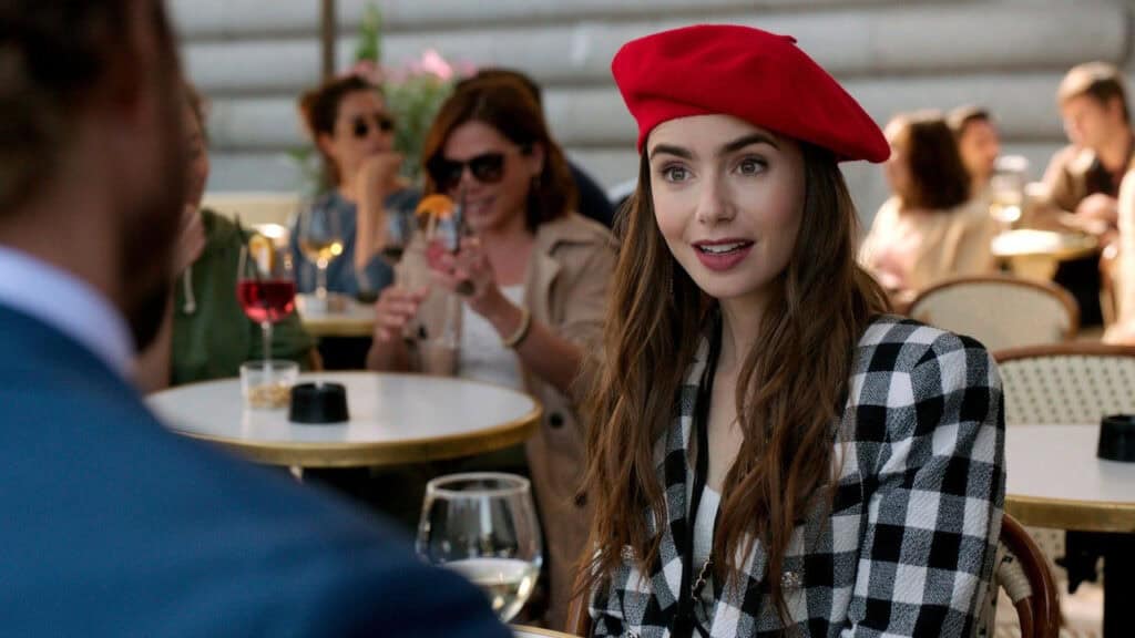 A woman wearing a red beret and patterned jacket seated at a Paris café, smiling during a conversation.