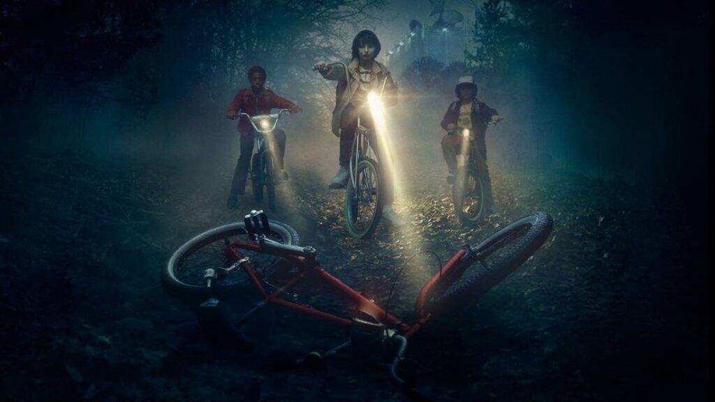 Three kids ride bicycles through a foggy forest at night, their flashlights cutting through the darkness in Stranger Things.
