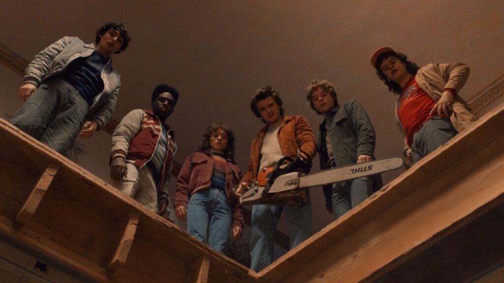 A group of teens peer downward into a dark opening from above, their expressions tense as danger waits below in Stranger Things.