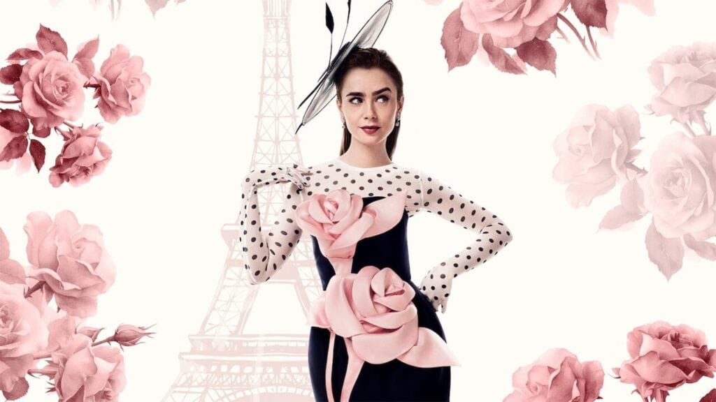 A stylish woman in a black dress with oversized pink floral details posing in front of a soft Paris-inspired background.