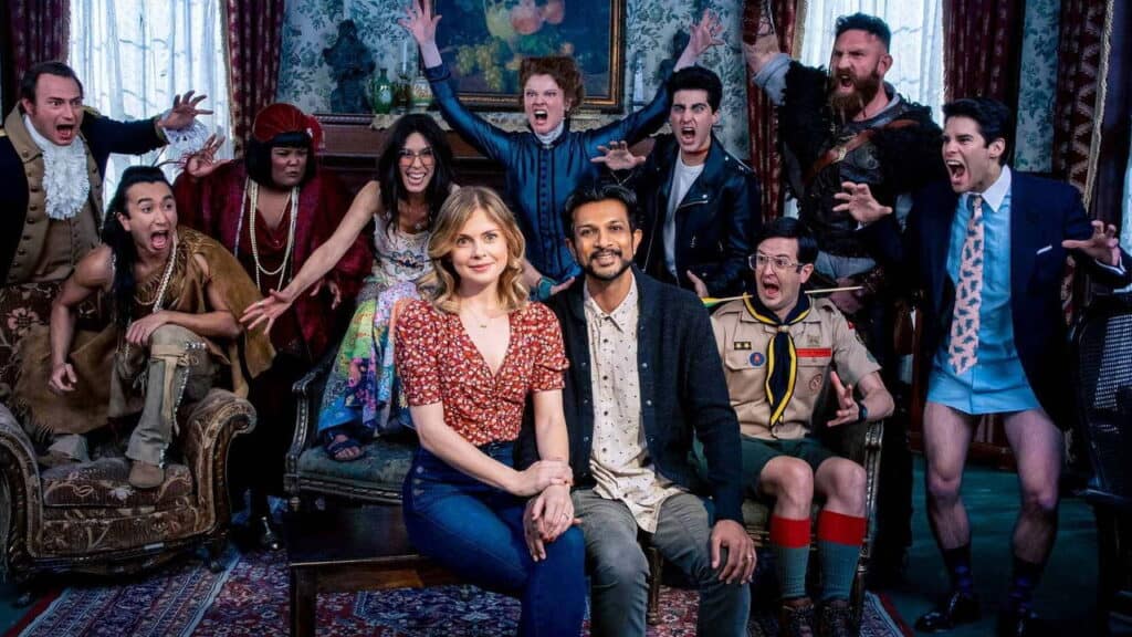 The living couple sit calmly on a couch while the ghosts behind them react dramatically, filling the room with exaggerated expressions.