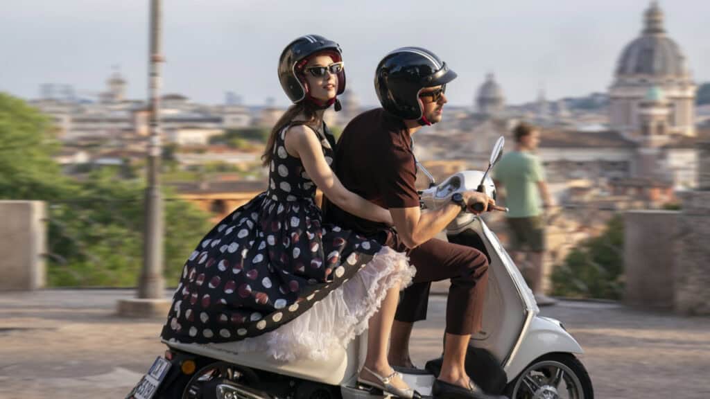 A couple riding a scooter through Paris with the city skyline visible in the background.