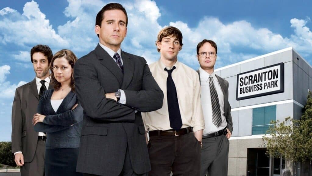 Main cast of The Office standing outside an office building labeled Scranton Business Park under a cloudy sky