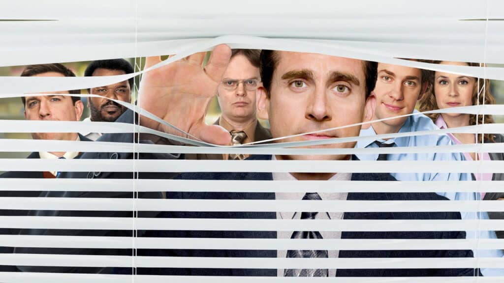 Office employees peering through horizontal blinds with one person in the foreground facing the camera
