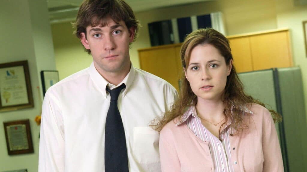 Two coworkers standing side by side inside a cubicle office, looking directly at the camera with serious expressions