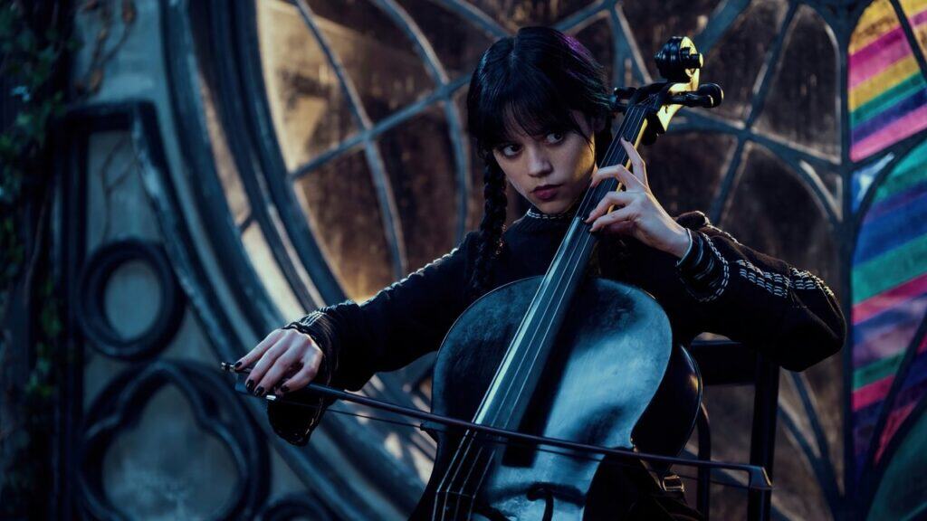 Wednesday Addams playing the cello in a stained-glass room at Nevermore Academy