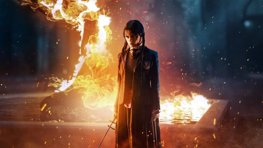Wednesday Addams standing calmly as flames burn behind her at Nevermore Academy