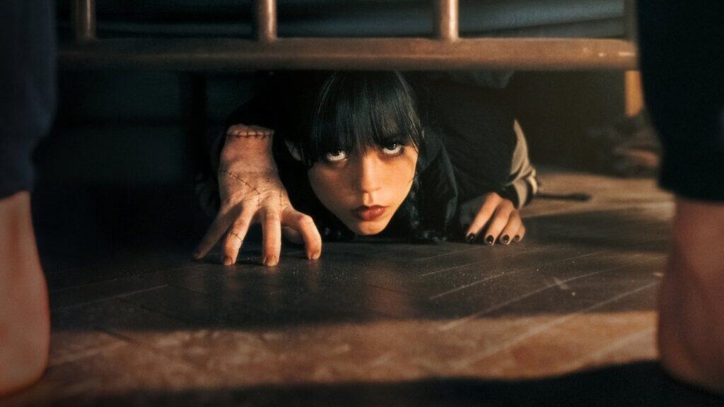 Wednesday Addams crawling on the floor in a dark, tense scene from the series