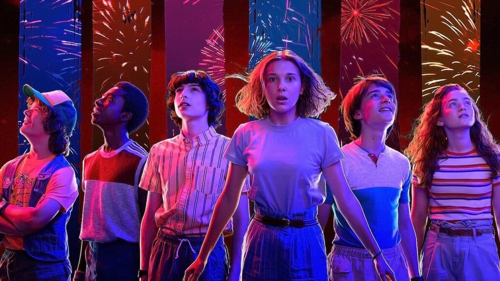 A group of friends look up in shock as fireworks light the night sky, blending awe and fear in Stranger Things.