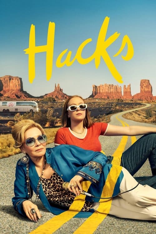 Promotional image for the show Hacks featuring Jean Smart and Hannah Einbinder lounging on a desert road with a tour bus and mountain buttes in the background.