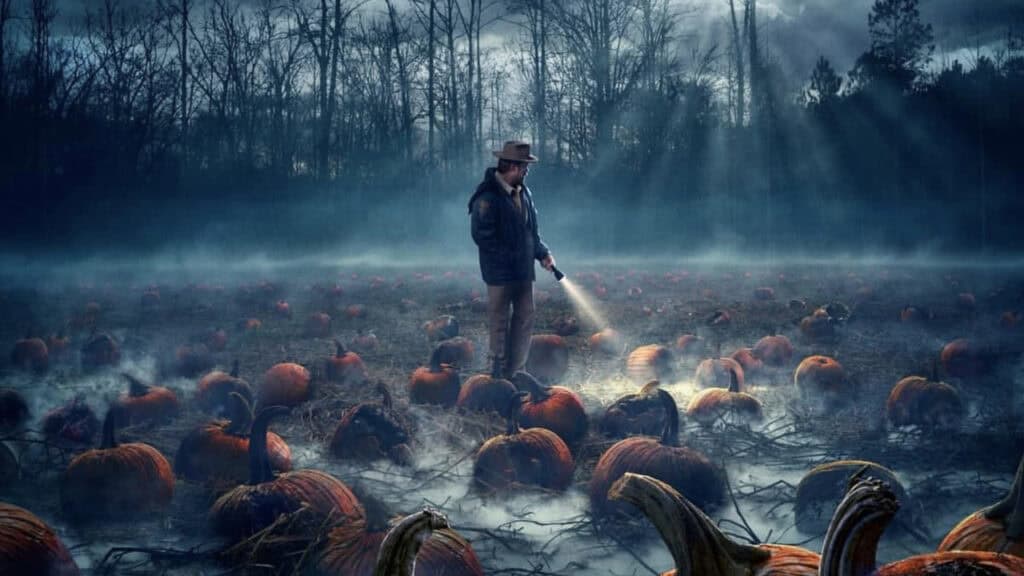 A man walks through a fog-covered pumpkin field at night while shining a flashlight on the ground in Stranger Things.