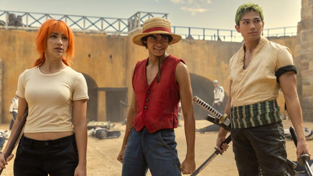 One Piece live action characters standing confidently in a sandy arena with defeated enemies in the background