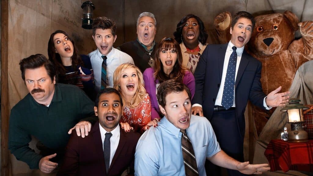 The ensemble cast of Parks and Recreation reacting with exaggerated expressions in a comedic scene, showing the show’s energetic and expressive humor style.