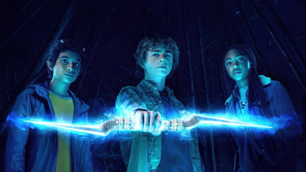 Percy Jackson holds a glowing blue sword surrounded by magical energy while Annabeth and Grover stand behind him