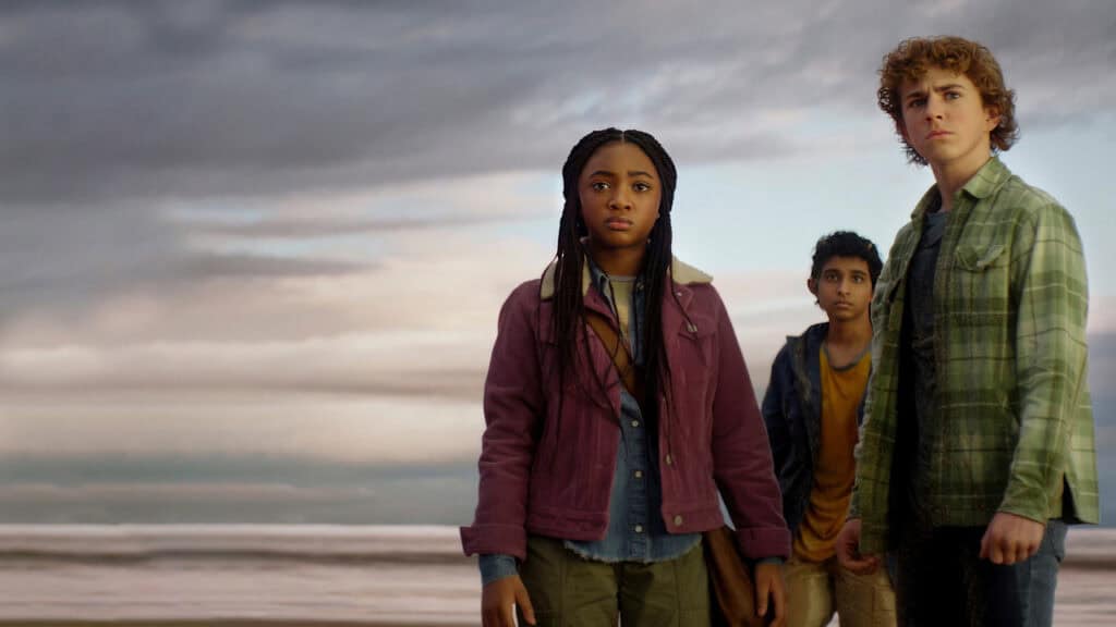 Percy Jackson stands beside Annabeth and Grover on a beach as dark clouds gather over the ocean