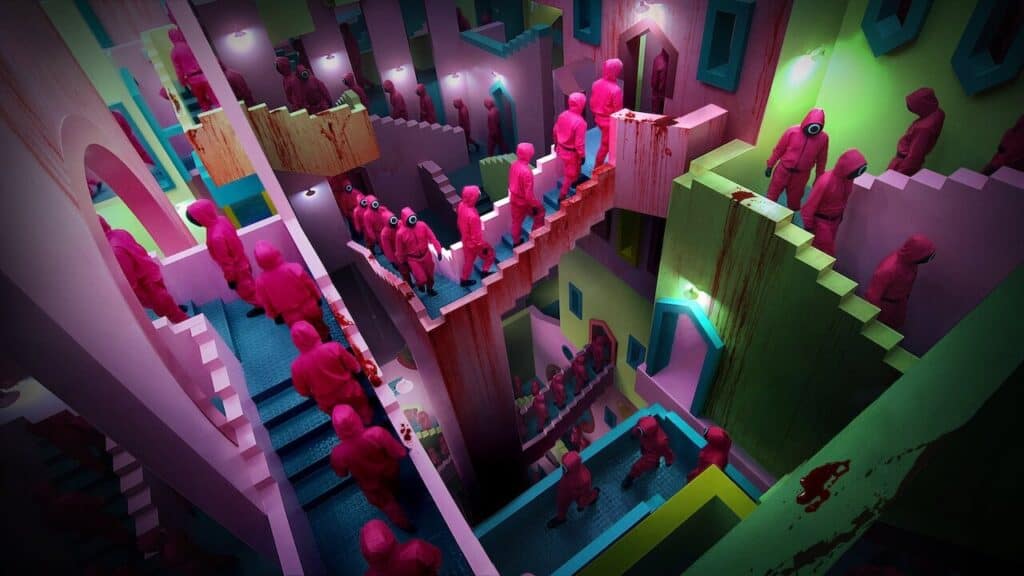 Contestants in pink guard uniforms walk through a bright, maze-like staircase structure inside the Squid Game facility, symbolizing the confusing and controlled system of the competition.