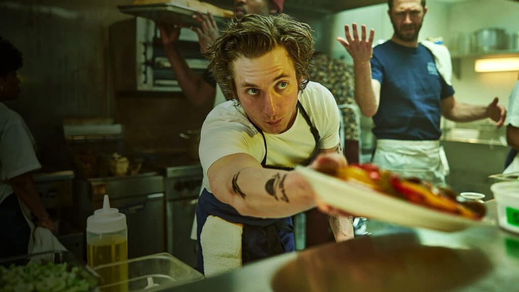 Carmy rushes a plated dish across a chaotic kitchen during a stressful service in The Bear.