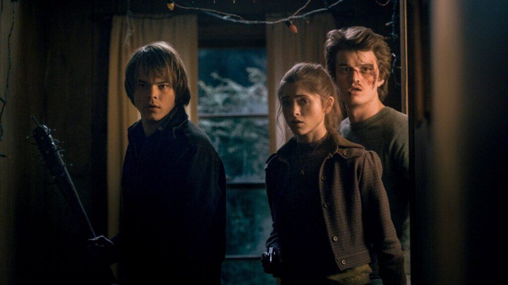 Three teenagers stand inside a dimly lit house, visibly injured and tense, reacting to an unseen threat as the consequences of their battle with the supernatural become clear.