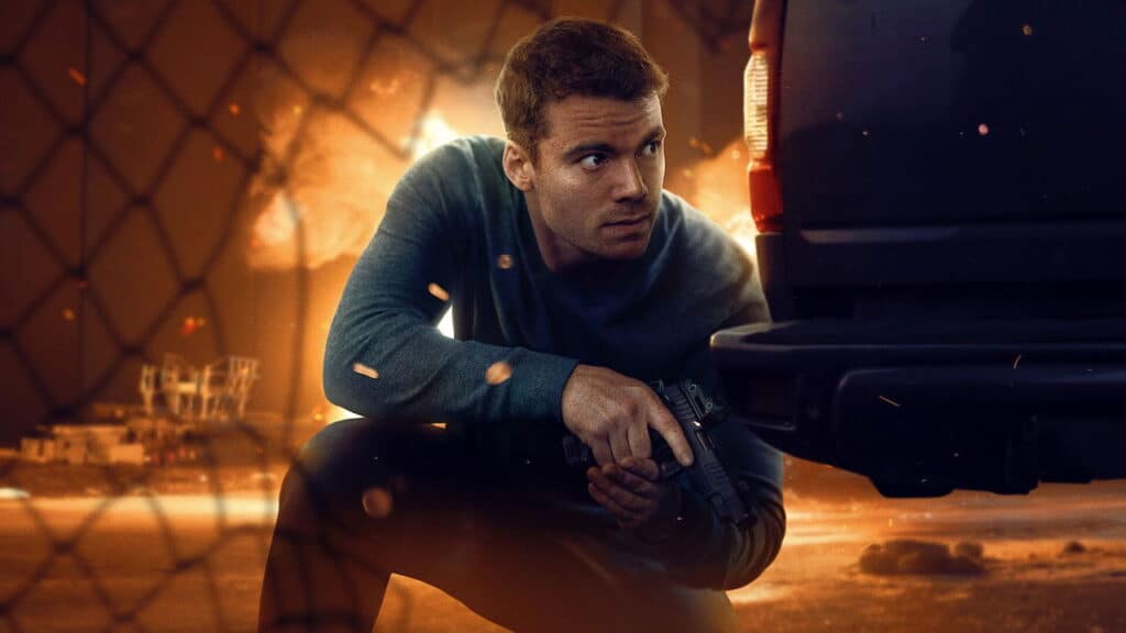 A man crouching behind a vehicle holding a gun as sparks fly during an intense action scene in The Night Agent