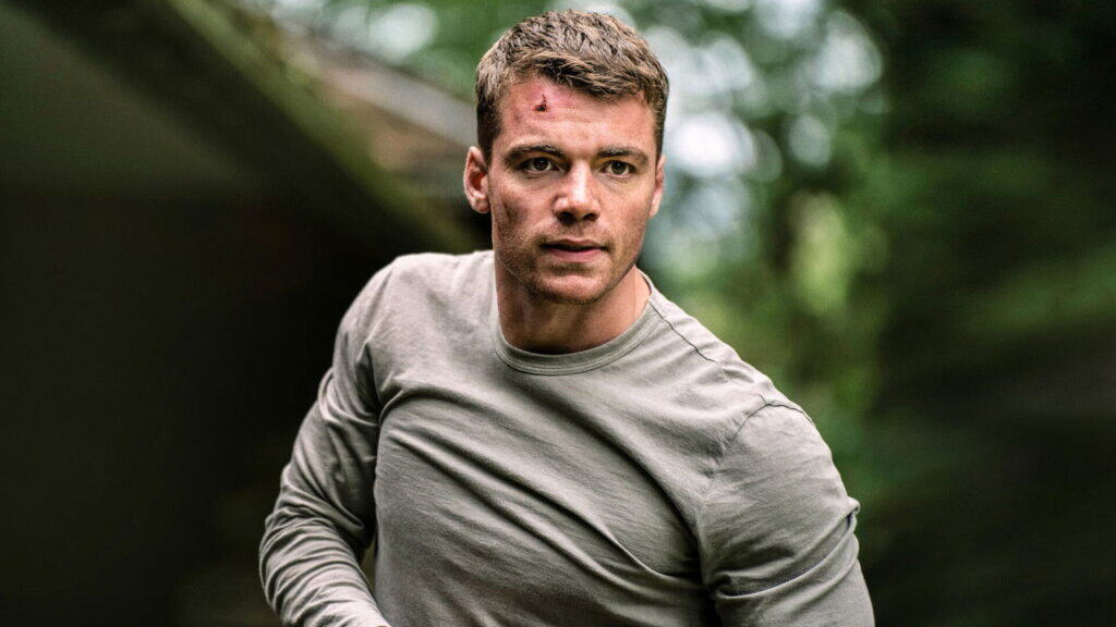 A man with a cut on his forehead running through a wooded area during a tense chase in The Night Agent thriller series