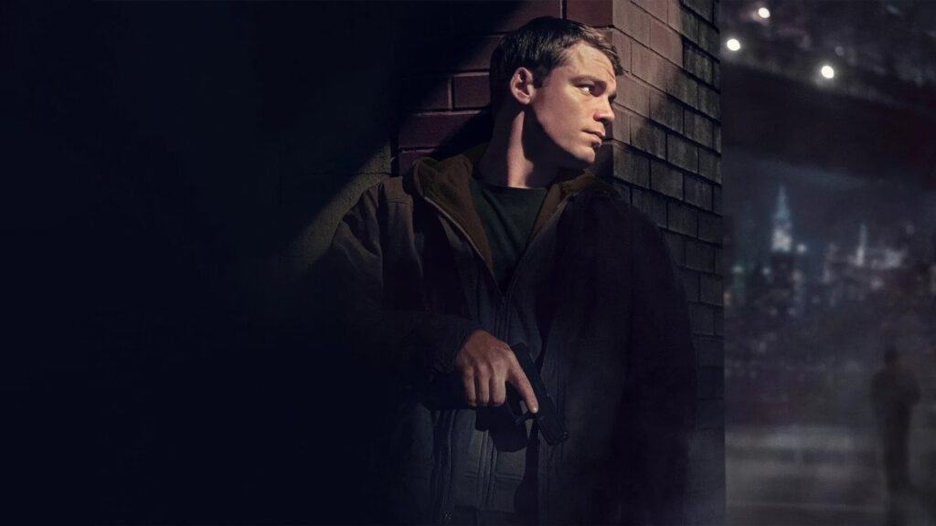 A man hiding against a brick wall at night while holding a gun in a suspenseful moment from The Night Agent series