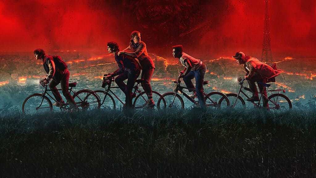 A group of kids ride bicycles across a glowing red sky landscape as a massive shadow looms behind them in Stranger Things.