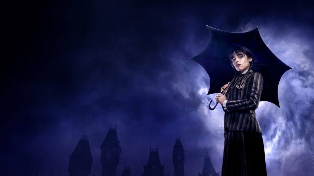 Wednesday Addams holds a black umbrella while standing in a stormy, gothic setting with towering silhouettes behind her.