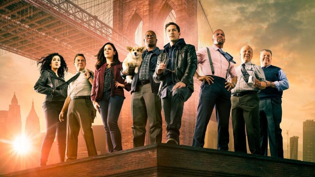 The main ensemble cast of Brooklyn Nine-Nine standing heroically on a rooftop in front of the Brooklyn Bridge at sunset, featuring Jake Peralta, Captain Holt, Amy Santiago, and the squad.