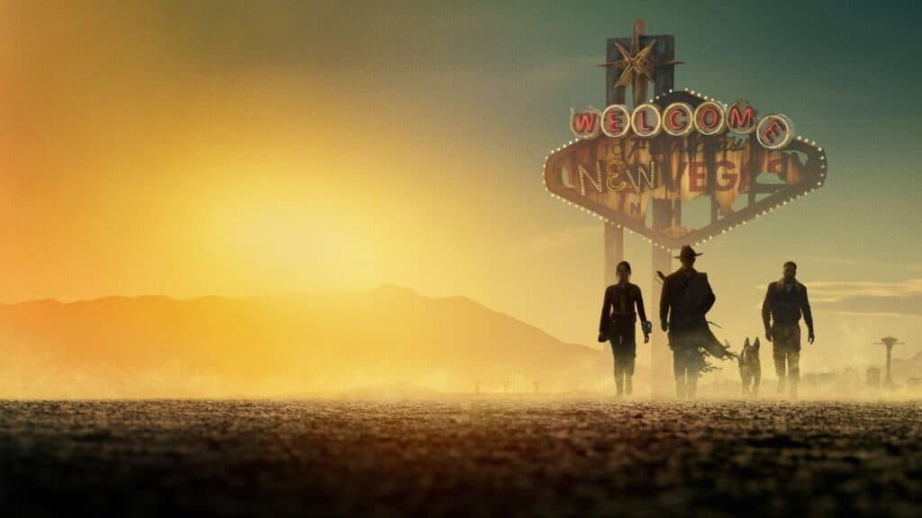 Wide scene from Fallout showing Lucy, The Ghoul, Maximus, and Dogmeat walking through the desert near the Welcome to New Vegas sign at sunset.